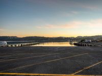 a long empty parking lot with a lake and a mountain in the background at sunset