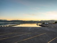 a long empty parking lot with a lake and a mountain in the background at sunset