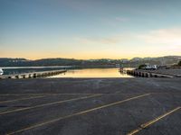 a long empty parking lot with a lake and a mountain in the background at sunset