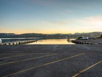 a long empty parking lot with a lake and a mountain in the background at sunset