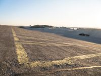 an empty road with lines painted in the sand near a beach and ocean with cars going to a left