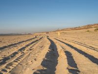 a large sandy area with tire tracks on it and some people walking in the distance