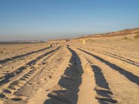 a large sandy area with tire tracks on it and some people walking in the distance