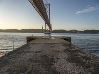 large bridge over water with sky and mountains in background and light from the sun setting