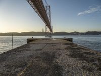 large bridge over water with sky and mountains in background and light from the sun setting