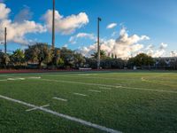 a soccer field has white lines on it and is green grass and tall poles in the distance