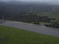 a skateboard on a hilly green slope next to trees and mountains as the sun is setting