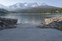 a pathway leading to a lake with snow capped mountains behind it and an out dock across the water