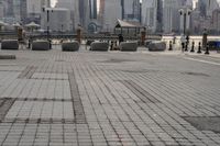 a paved park with benches next to a water body and a skyline of high rises in the background
