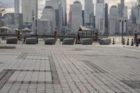 a paved park with benches next to a water body and a skyline of high rises in the background