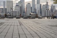 a paved park with benches next to a water body and a skyline of high rises in the background