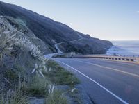 a highway leading into the middle of a valley near the ocean with a lone white car in the foreground