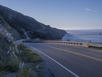 a highway leading into the middle of a valley near the ocean with a lone white car in the foreground