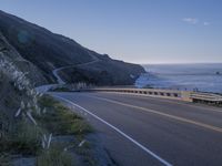 a highway leading into the middle of a valley near the ocean with a lone white car in the foreground