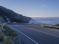 a highway leading into the middle of a valley near the ocean with a lone white car in the foreground