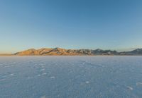 a white snow field with mountain range in the background and blue sky in the distance