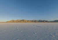 a white snow field with mountain range in the background and blue sky in the distance