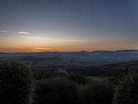 this is a sunrise over an italian countryside scene with a hill and forest in the background