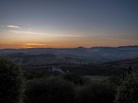 this is a sunrise over an italian countryside scene with a hill and forest in the background