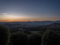 this is a sunrise over an italian countryside scene with a hill and forest in the background