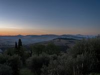 this is a sunrise over an italian countryside scene with a hill and forest in the background