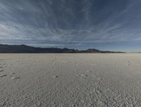 a large open desert with mountains in the background with snow on them, blue skies and clouds