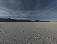 a large open desert with mountains in the background with snow on them, blue skies and clouds