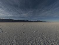 a large open desert with mountains in the background with snow on them, blue skies and clouds