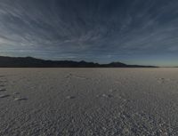 a large open desert with mountains in the background with snow on them, blue skies and clouds