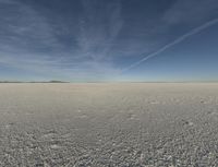 a desert area with a white substance and some clouds in the sky and a person running on the ground