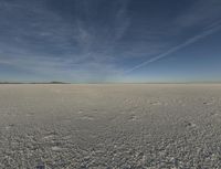 a desert area with a white substance and some clouds in the sky and a person running on the ground