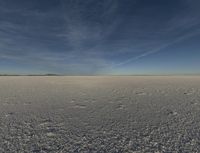 a desert area with a white substance and some clouds in the sky and a person running on the ground