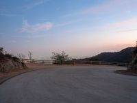 a curved road with the city skyline in the distance in a hilly area at dusk