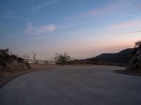 a curved road with the city skyline in the distance in a hilly area at dusk