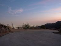 a curved road with the city skyline in the distance in a hilly area at dusk