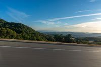 a man that is on a motorbike going down the road with hills and trees in the background