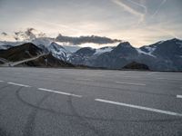 a snow covered road with mountains in the background at sunset with a white painted over line in the foreground