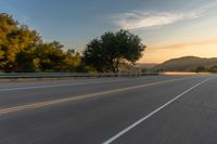 the front of a motorcycle going down a road at sunrise over a mountain and forest