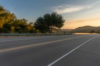 the front of a motorcycle going down a road at sunrise over a mountain and forest