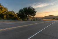 the front of a motorcycle going down a road at sunrise over a mountain and forest