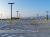 an empty parking lot with a number of lights on the poles and yellow poles around it