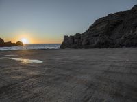 a large rock in a body of water at sunset with a person on it doing tricks on the beach