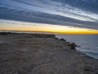 a bench sits on a rocky ledge near the sea and rocks at sunset above water