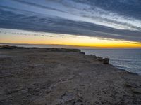 a bench sits on a rocky ledge near the sea and rocks at sunset above water