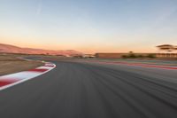 a photo of a dirt race track with sun setting in the distance of the track