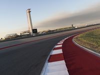 an empty racetrack with the view of a tower in the distance and green grass to the left