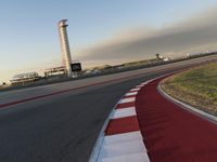 an empty racetrack with the view of a tower in the distance and green grass to the left