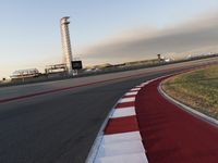 an empty racetrack with the view of a tower in the distance and green grass to the left