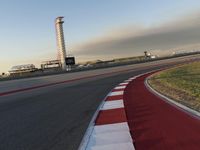 an empty racetrack with the view of a tower in the distance and green grass to the left