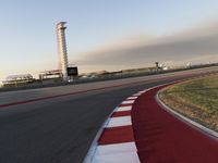 an empty racetrack with the view of a tower in the distance and green grass to the left